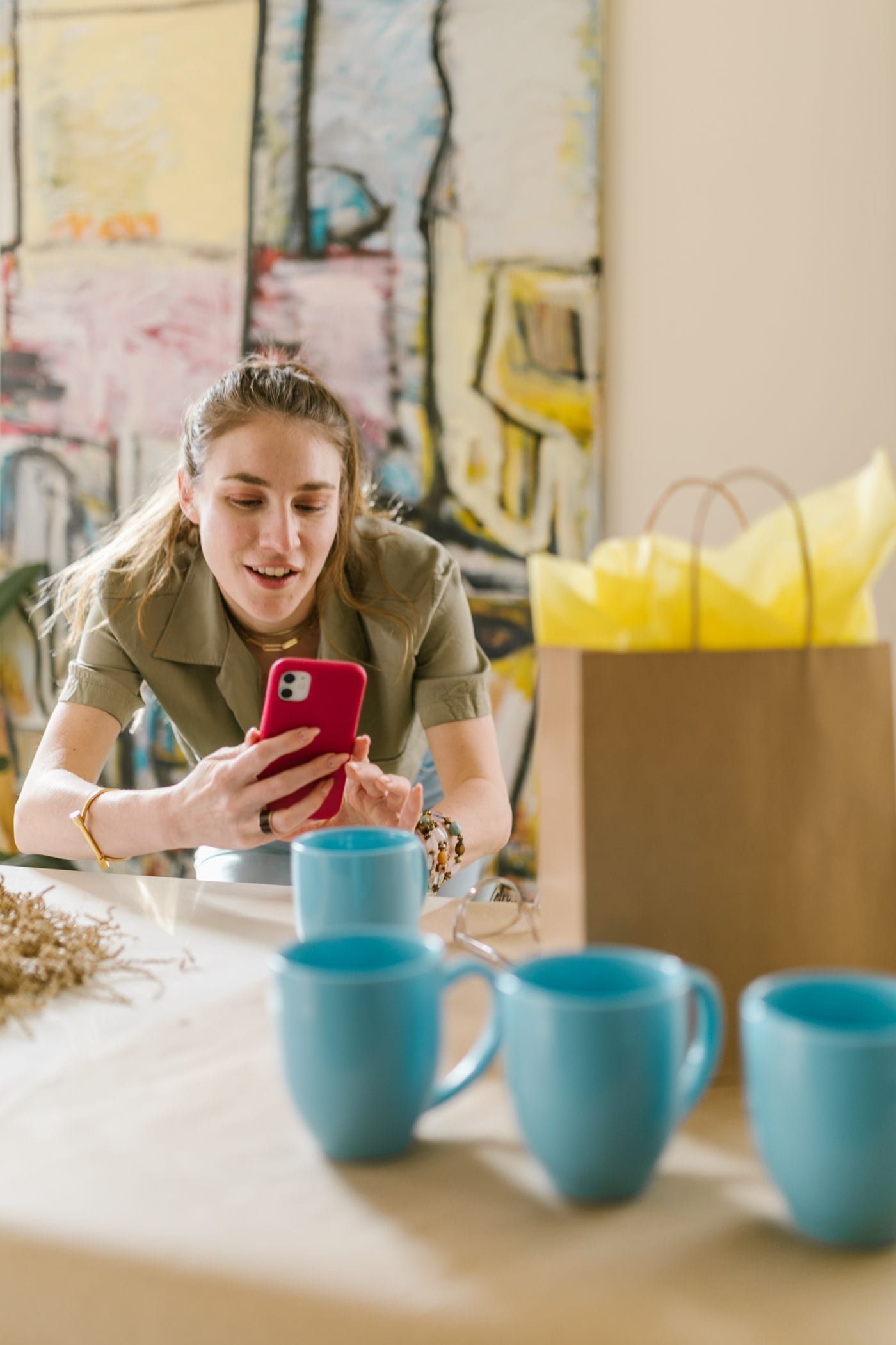 Mujer revisa pedidos en su celular rodeada de tazas y bolsas de su tienda