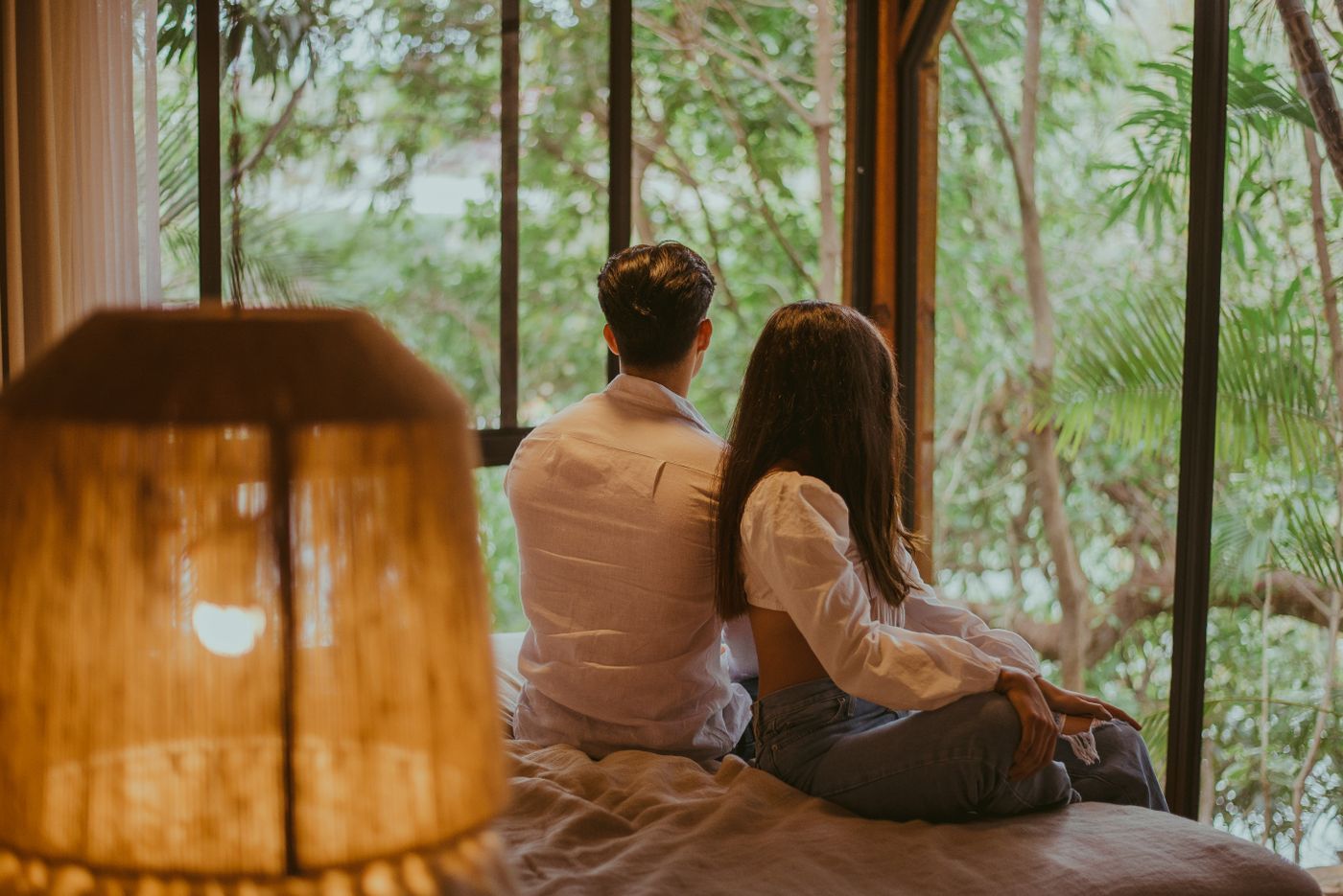 Una pareja mira la selva desde la cama de una cabaña con ventanales