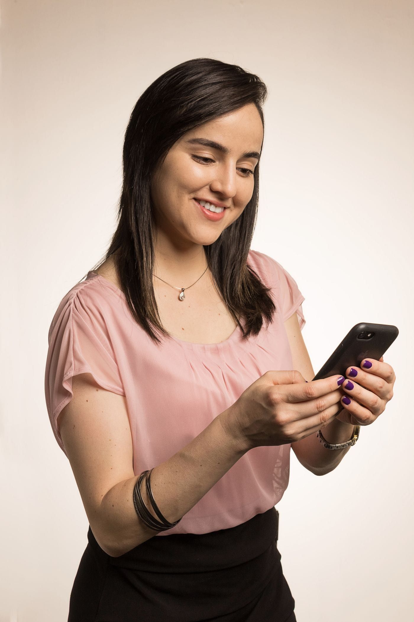 Una mujer sonríe mientras responde mensajes de clientes en su celular